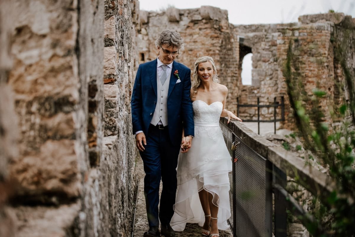 Sposi mano nella mano sul camminamento delle mura di un castello sul Lago di Garda
