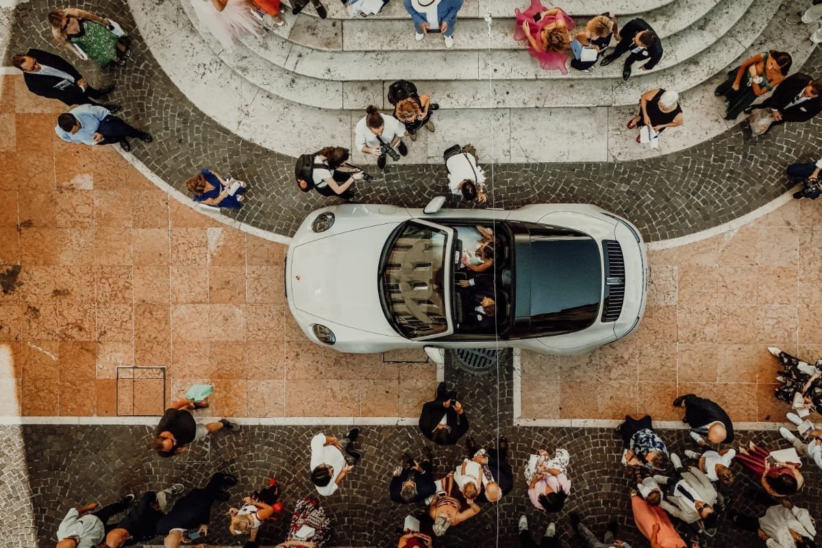 Vista dall’alto dell’auto sportiva degli sposi circondata dagli invitati in piazza