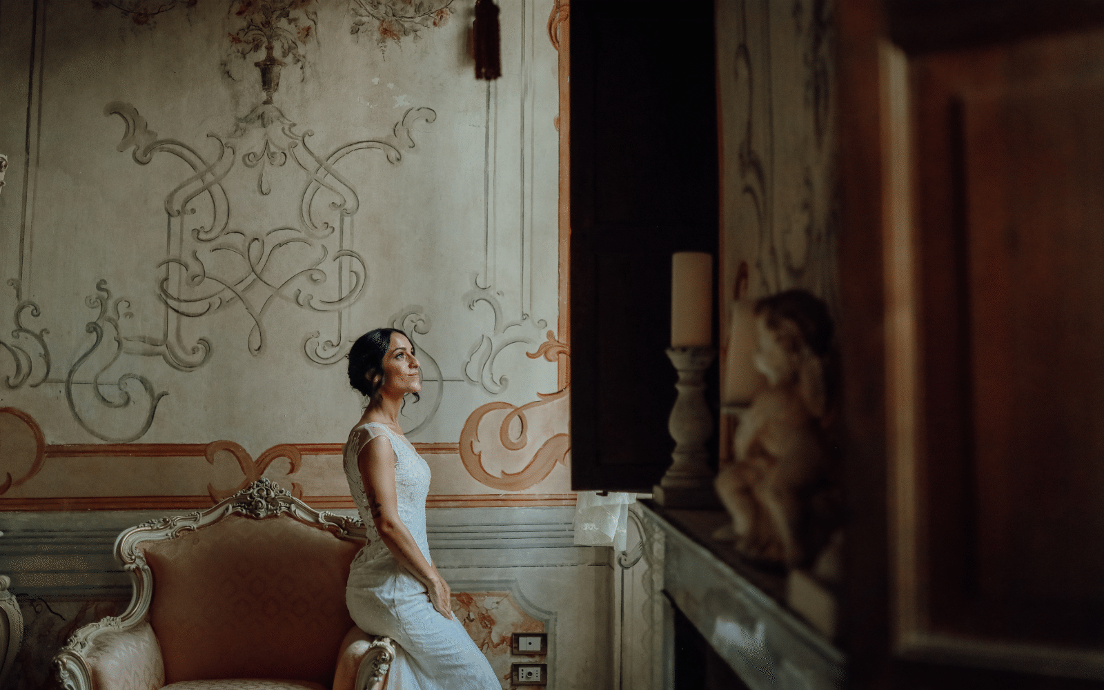 Sposa in abito aderente nella sala affrescata di una villa, accanto alla finestra