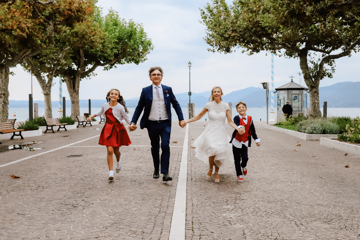 Newlyweds running hand in hand with their children along the lakeside of Lake Garda, photo by Camilla Lovato