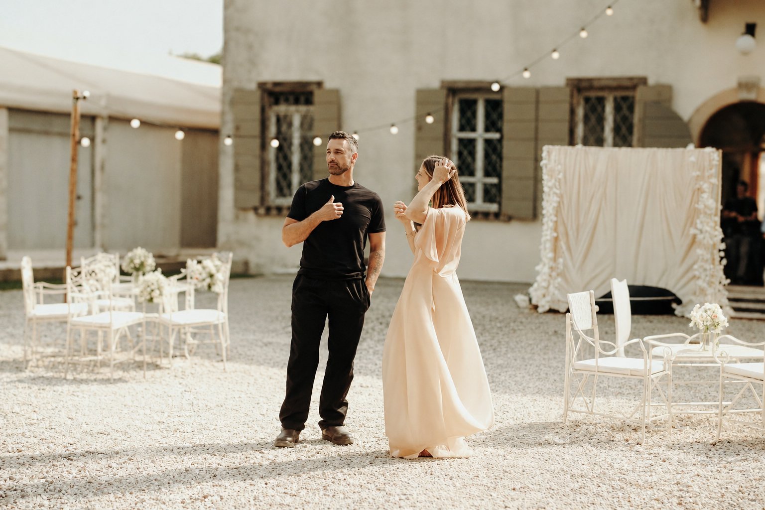 Raoul Bova with a woman in a long powder-pink gown in the courtyard of a villa set up for a wedding, photo by Camilla Lovato