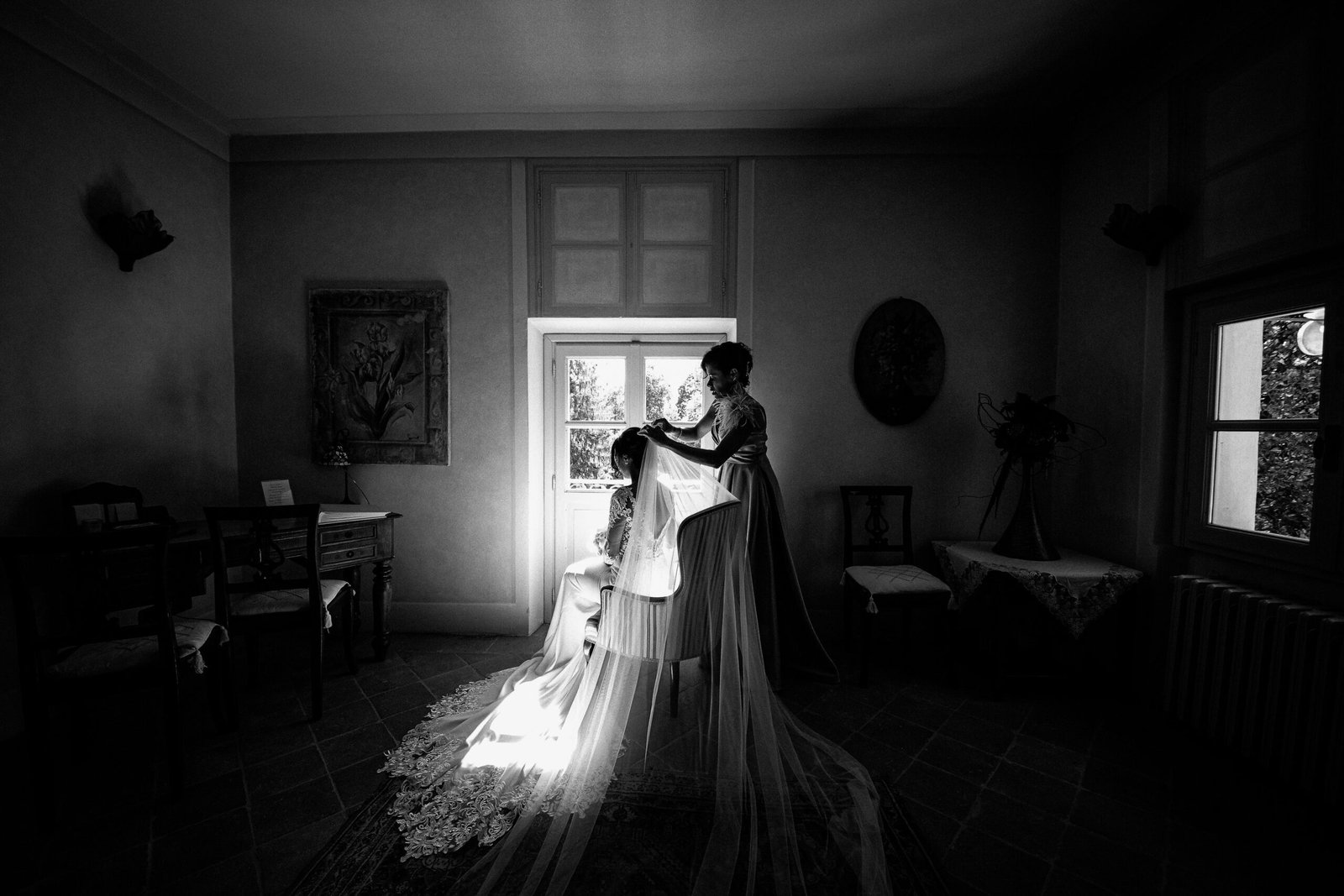 Sposa aiutata a sistemare il velo davanti alla finestra, in bianco e nero