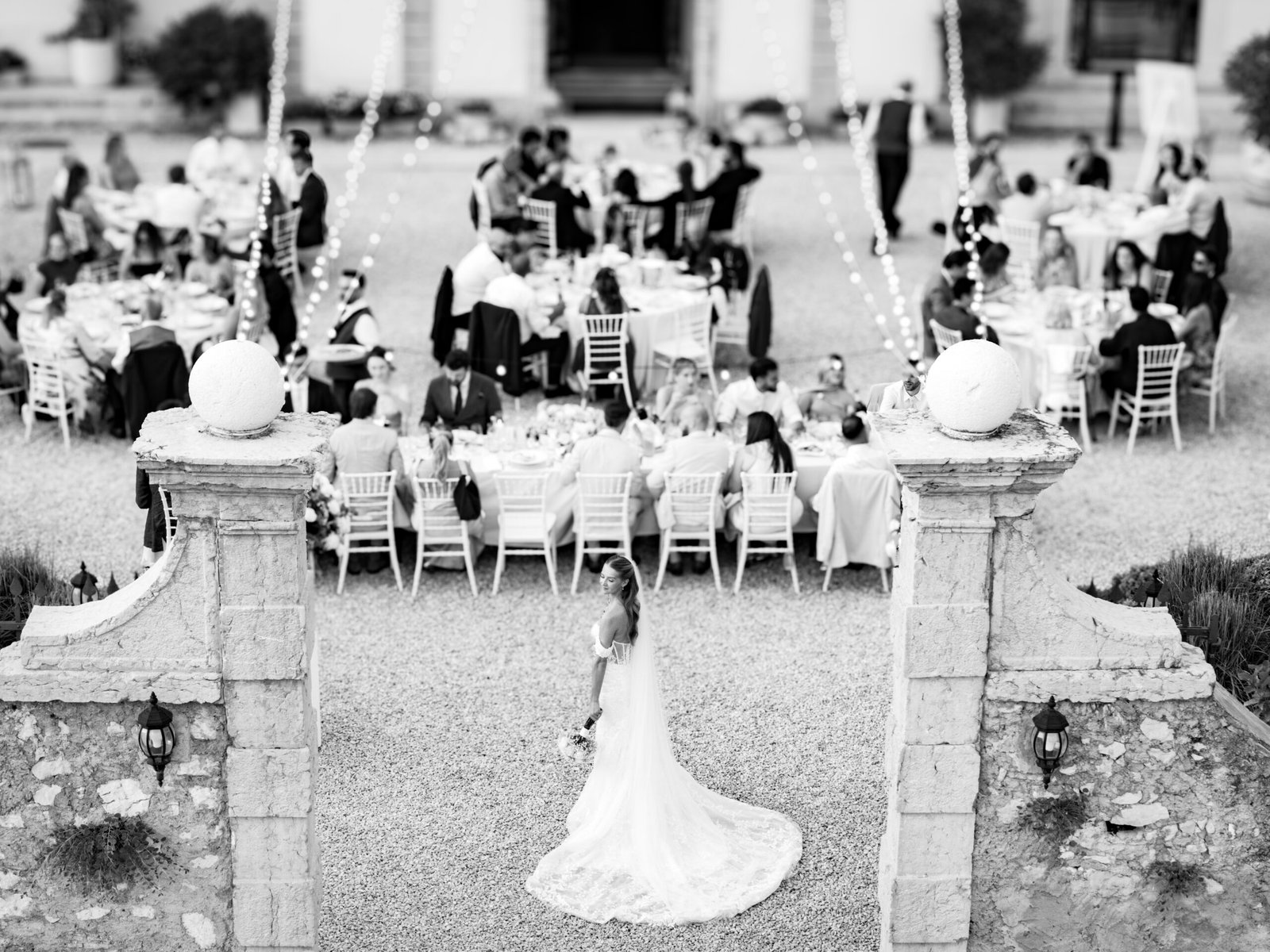 Bride seen from above entering the reception courtyard between the set tables, in black and white