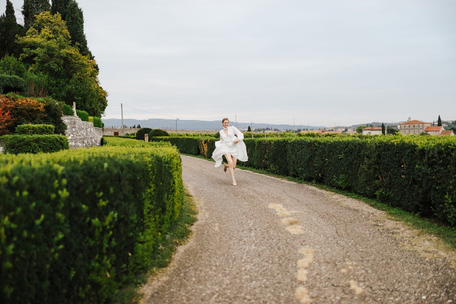 Sposa che corre lungo un viale di siepi nel parco di una villa
