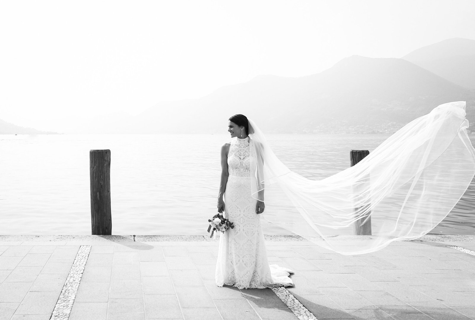 Sposa con il velo al vento su un pontile del lago, in bianco e nero