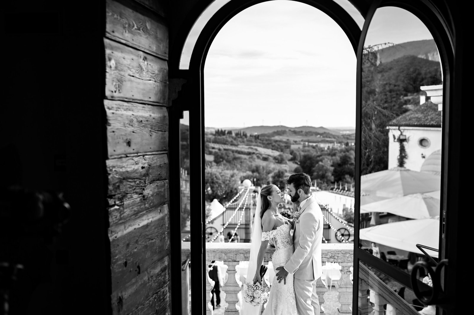 Bride and groom embracing, framed by an archway opening onto the terrace of Villa Cariola, in black and white