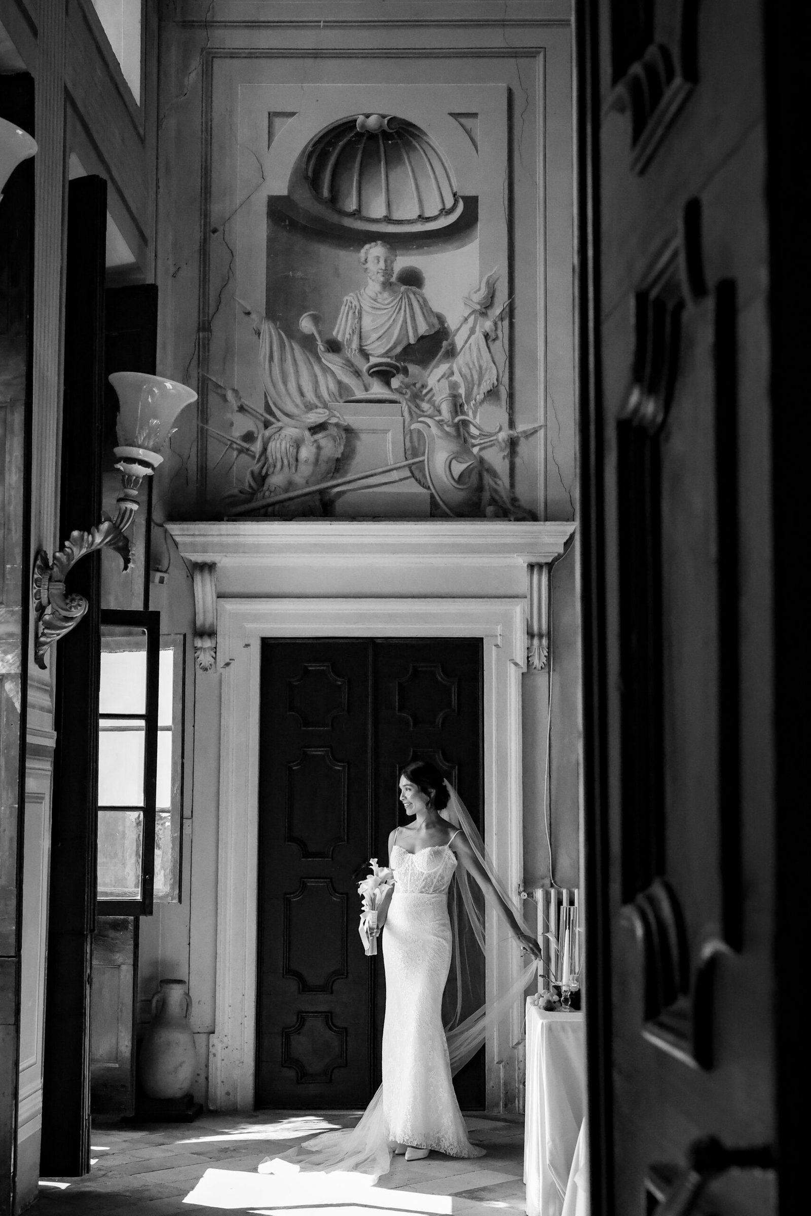 Bride standing in a doorway beneath a carved frieze, in black and white
