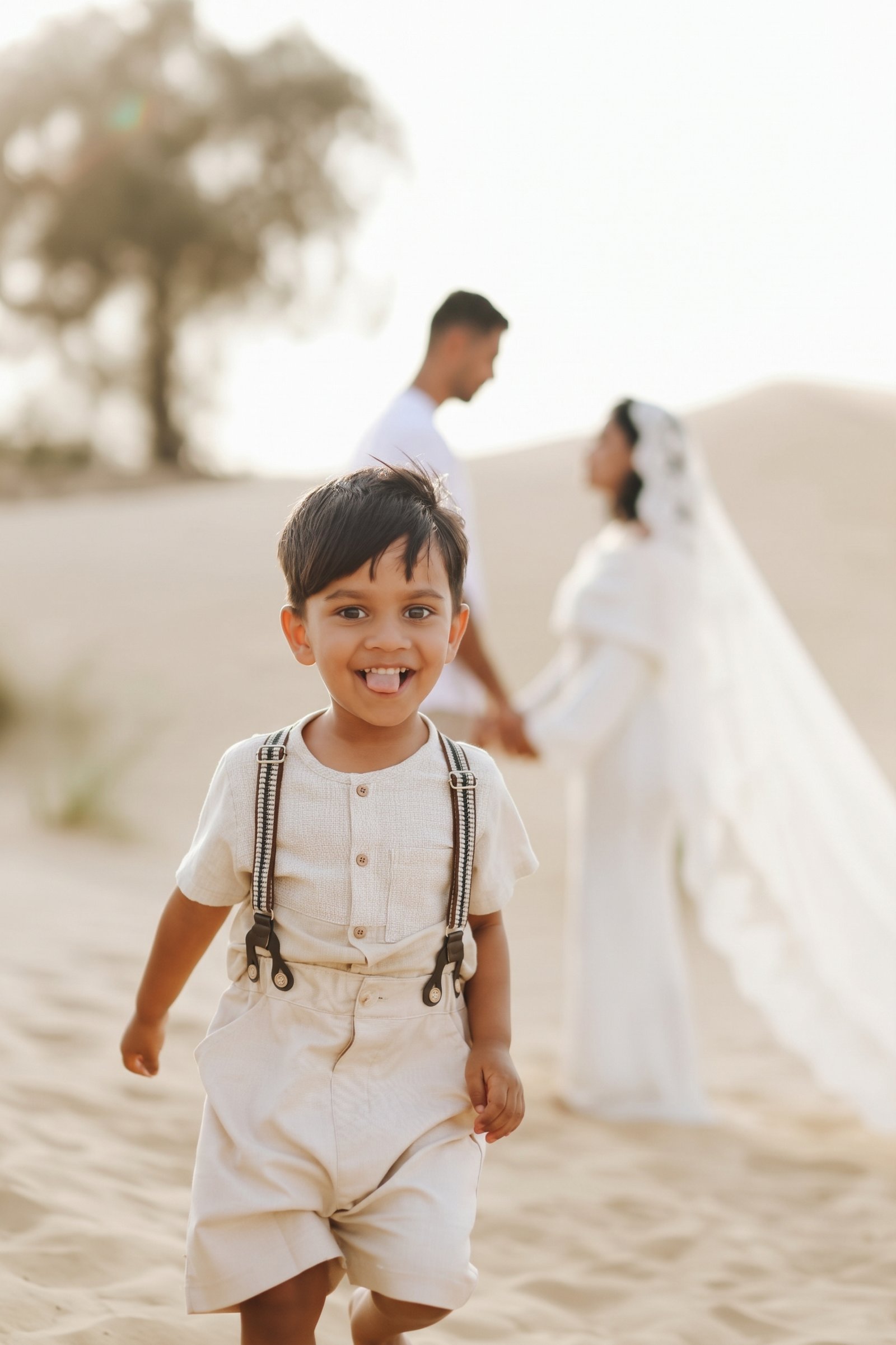 Smiling child in the foreground with the bride and groom holding hands on the dunes behind him
