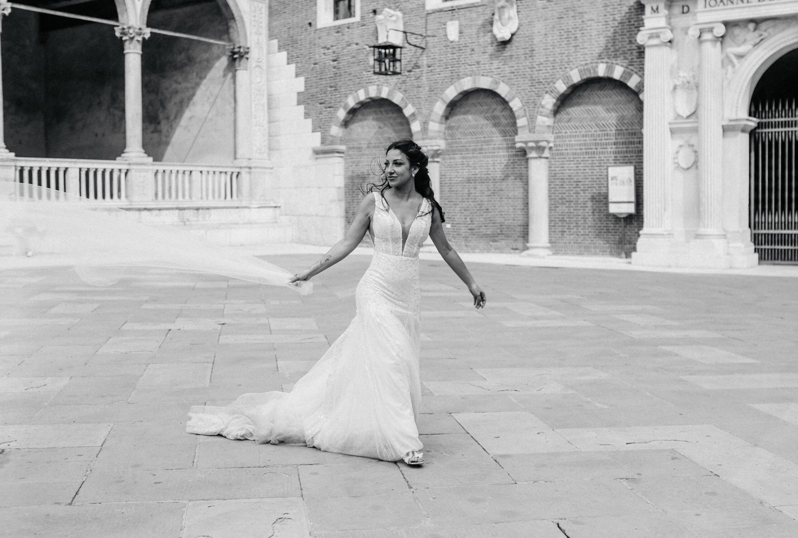 Sposa che danza nel cortile porticato di un palazzo storico, in bianco e nero