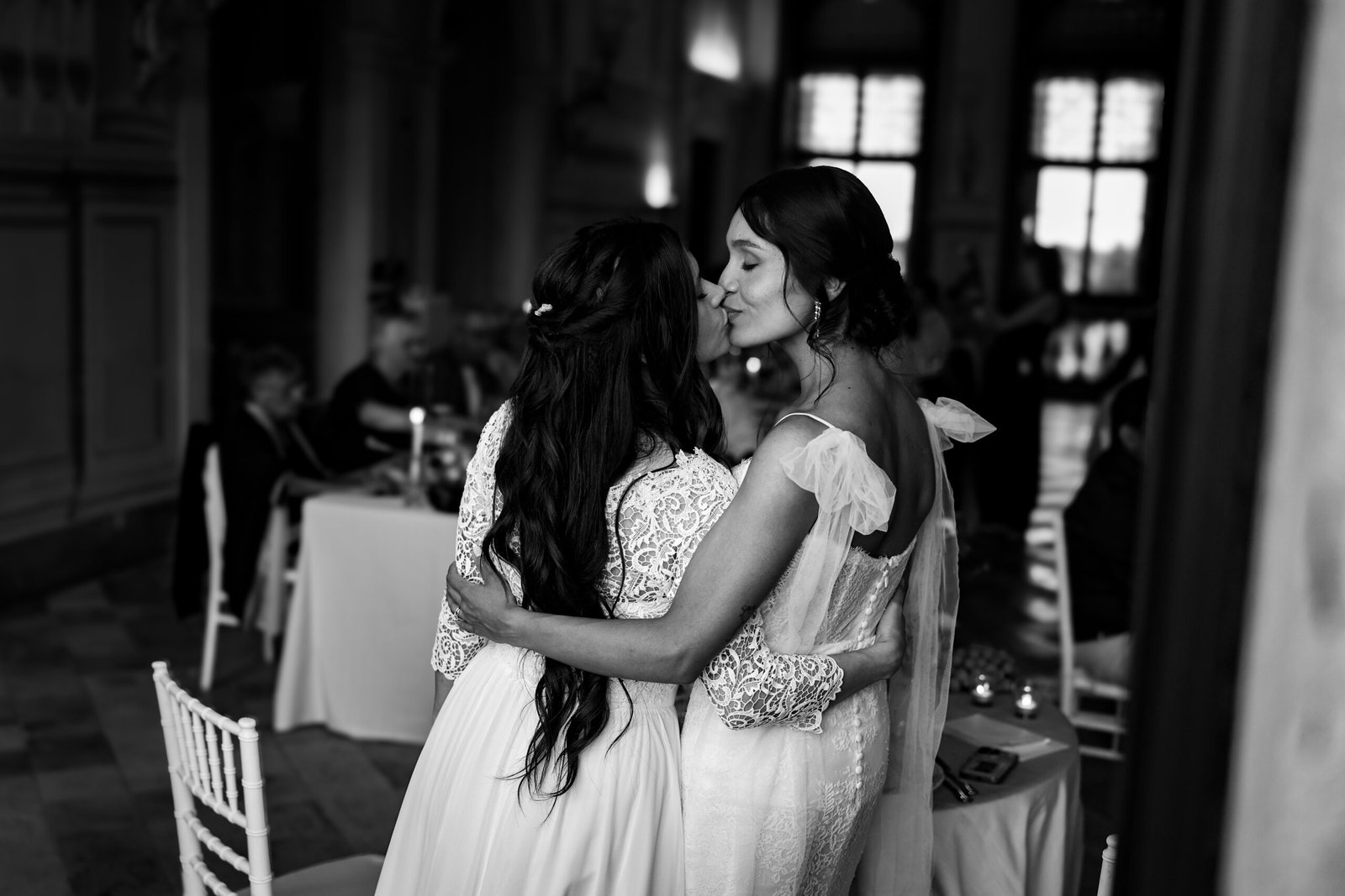 Two brides kissing in an embrace during the reception, in black and white
