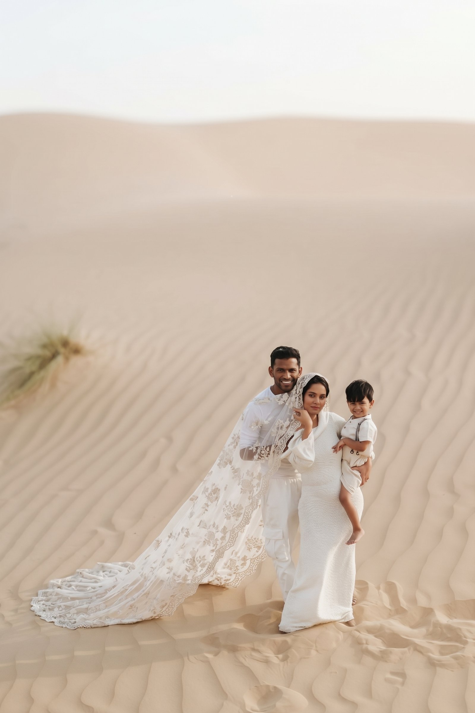Bride and groom holding their son in their arms among the sand dunes of the Dubai desert